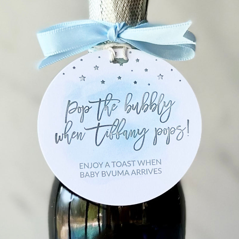blue watercolor baby shower tags are tied on to mini bottles of champagne inviting guests to raise a glass and cheer to the new parents when baby is born. Personalized with names of Mom and Baby, each handmade tag is made to order sourcing the highest quality supplies right here in the USA. Champagne is not included but easily sourced through your local liquor store.