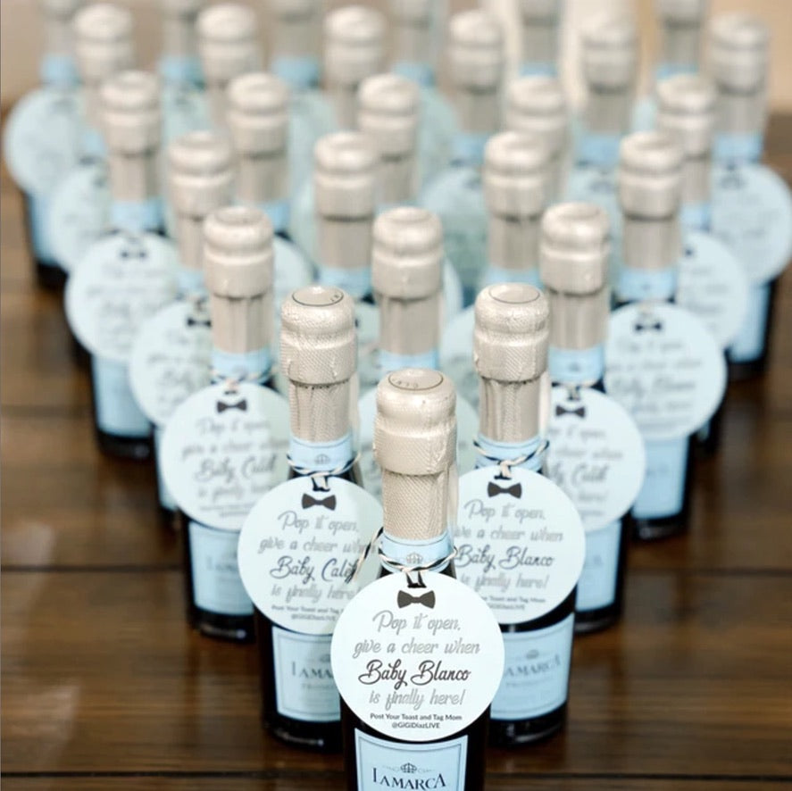 rows of mini champagne bottles in triangle form with small tags tied around the bottle neck reading pop it open give a cheer when baby blanco is finally here